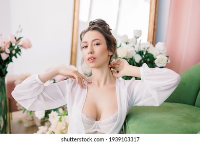 Portrait of a beautiful young girl with long hair in transparent peignoir posing among flowers in a stylish interior. Fresh flowers - roses, tulips. Morning of bride
