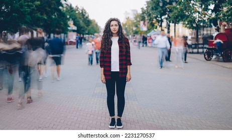 Portrait of beautiful young girl with long curly hair standing in street looking at camera when many men and women are walking around in hurry on summer day. - Shutterstock ID 2231270537
