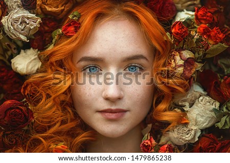 portrait of a beautiful young girl with red hair and freckles and blue eyes strewn with roses