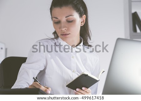 Portrait of beautiful young girl taking notes at her workplace. Computer and calculator are lying on her desk. Concept of statistician's work