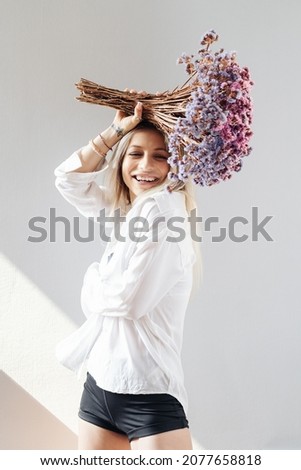 Portrait of a beautiful young girl in white shirt, black top and shorts, holding a big bouquet of dried flowers over gray background splashed by lines of light