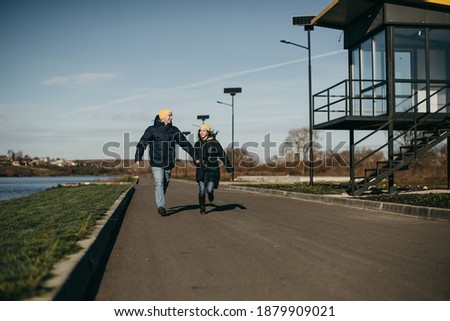 Portrait of a beautiful young happy couple man and woman in yellow hats, jackets having fun, running near modern glass architecture. Girlfriend, style, boyfriend, house. Running on the road near lake
