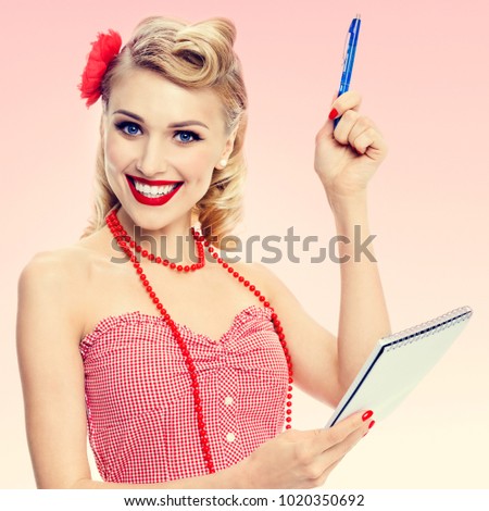 Portrait of beautiful young happy smiling woman with notepad, in pin-up style clothing, over pink background. Caucasian blond model posing in retro fashion and vintage concept studio shoot.