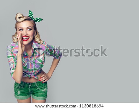 Portrait of beautiful young happy smiling woman, dressed in pin-up style. Caucasian blond model posing in retro fashion and vintage concept studio shoot, on grey background. Copyspace.