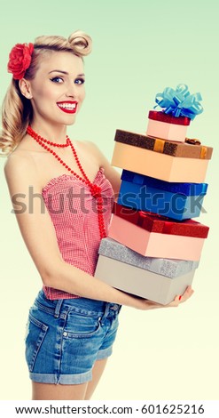 Portrait of beautiful young happy smiling woman in pin-up style clothing, holding gift boxes, on green background. Caucasian blond model posing in retro fashion and vintage concept shoot.