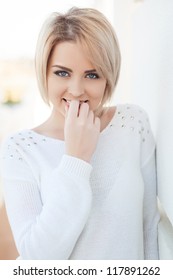 Portrait of a beautiful young and healthy women blonde with expressive eyes and a bob hairstyle. Poses in front of a white wall.