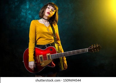 Portrait of beautiful young hipster woman with curly hair with red guitar in neon lights. Rock musician is playing electrical guitar. 90s style concept. - Powered by Shutterstock