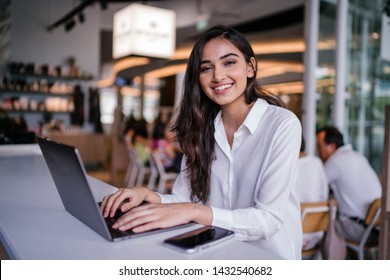 Portrait of a beautiful, young Indian Asian woman working on her laptop in a trendy coworking space. She is working in a technology startup and is young, vibrant and excited about her role.