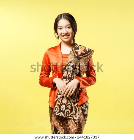 portrait of Beautiful young indonesian woman wearing modern kebaya kutu baru with batik shawl isolated on yellow background [[stock_photo]] © 