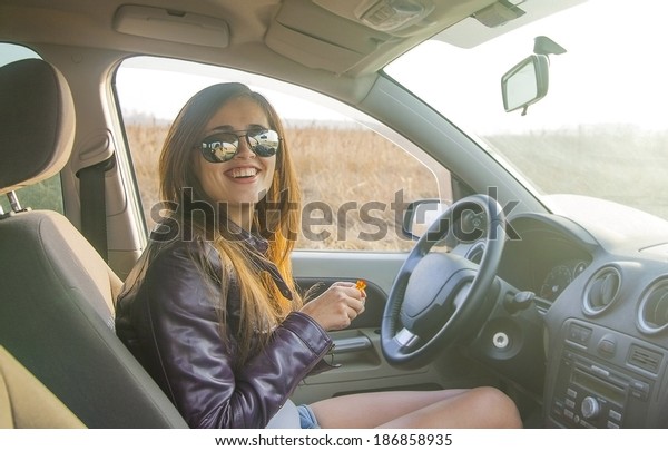 Portrait of beautiful young latin hispanic brunette\
woman in  new car  indoor and smiling and looking at  passengers in\
back seat. The idea of taxi driver Cute girl in sunglasses with\
candy