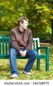 Portrait Of Beautiful Young Man In The Autumn Park Sitting On Bench