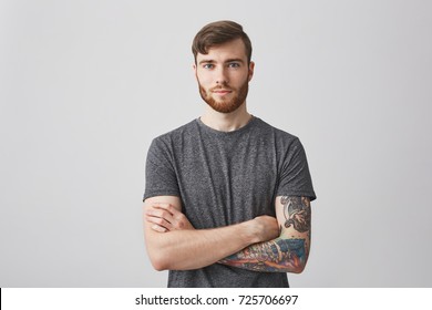 Portrait of beautiful young man with ginger beard and tattooed hand looking in camera with gentle smile and calm expression.