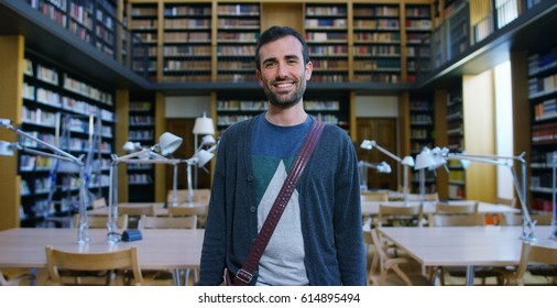 Portrait of a beautiful young man smiling happy in a library holding books after doing a search and after studying. Concept: educational, portrait, library, and studious. - Shutterstock ID 614895494