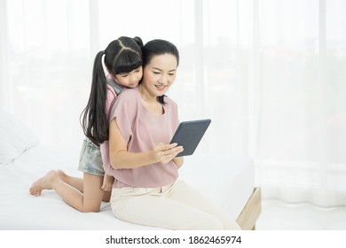 Portrait Of Beautiful Young Mom With Girl Sitting On The Bed In A Moment Of Intimacy While Buying Products Online With Tablet,
Social Distancing And Online Education Concept.