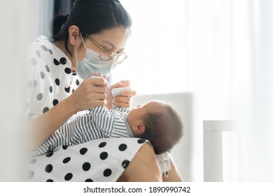 Portrait Of Beautiful Young Mom Wearing Protective Face Mask Playing With Baby Boy In Bedroom. Asian Mother Holding Newborn Child Hands. Happy Mother’s Day. Covid-19 Or Cororavirus Pandemic