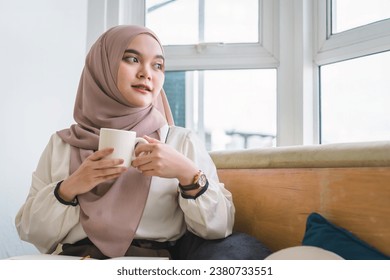 Portrait of beautiful young Muslim woman drinking coffee while sitting and relaxing in the cafe - Powered by Shutterstock