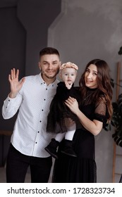 Portrait Of Beautiful Young Parents And Their Cute Little Daughter Hugs, Looking At Camera And Smiling Indoors. Mother's, Father's, Baby's Day. Concept Of Family. Family Look