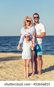 Portrait of beautiful young parents and their cute little daughter in casual clothes and sun glasses looking at camera and smiling, standing on the sunny beach - Shutterstock ID 453656815