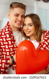 Portrait of beautiful young people. They are happy together, hugging each other and throwing blanket over their shoulders, celebrating Valentine's Day with glasses of wine and red airy heart. Love .