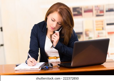 portrait of beautiful young secretary working from desk talking on cell phone