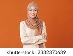 portrait of beautiful young smiling muslim woman in traditional religious hijab on orange background
