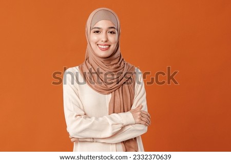 portrait of beautiful young smiling muslim woman in traditional religious hijab on orange background
