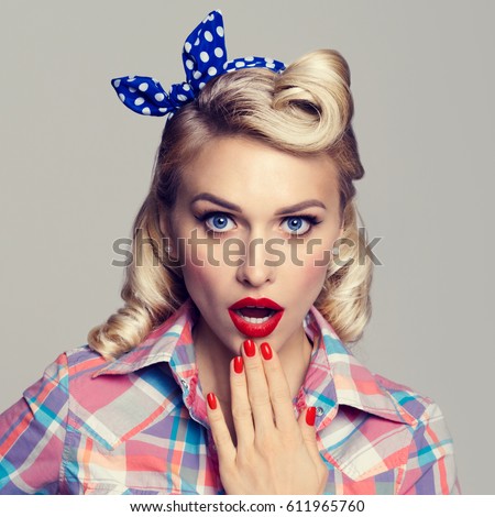 Portrait of beautiful young surprised woman, dressed in pin-up style. Caucasian blond model posing in retro fashion and vintage concept studio shoot, on grey background.