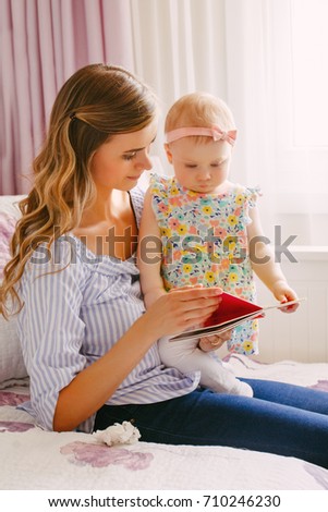 Portrait of beautiful young white Caucasian mother and little girl daughter reading book together indoors at home. Parent with child doing family activity. Lifestyle concept