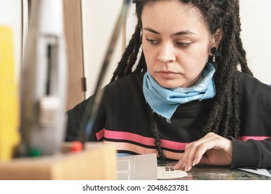 Portrait Of Beautiful Young White Girl Hispanic Latina Art Director, With Dreadlocks And Pretty Eyes, Sitting, In Her Studio, Working On A Model With Styrofoam, Onion Paper And Tools On Her Table.