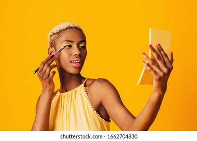 Portrait Of A Beautiful Young Woman Applying Yellow Eye Shadow Make Up To Her Eyes And Holding Compact Mirror