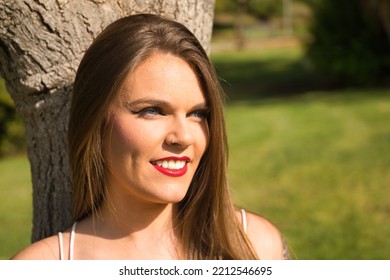 Portrait Of Beautiful Young Woman, Blonde, Blue Eyes, Leaning Against A Tree Trunk In An Outdoor Park On A Sunny Day. Concept Beauty, Fashion, Model, Nature, Spring.