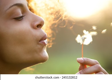 Portrait of a beautiful young woman blowing dandelion flower