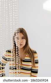 Portrait Of Beautiful Young Woman In Bright Living Room With White Walls And Iridescent Curtain