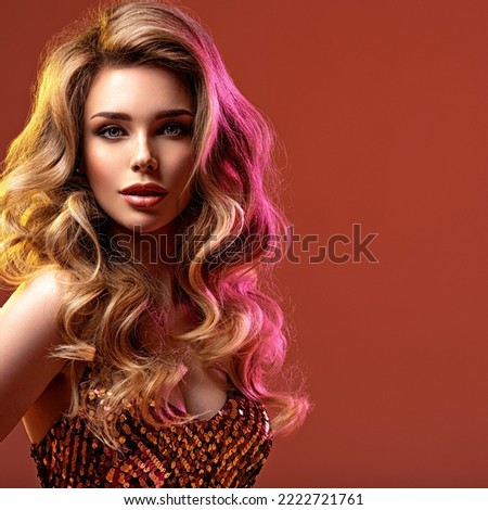 Portrait of beautiful young woman with bright shiny makeup. Blonde with brightly colored long hair. Pretty girl with long curly hair.   Fashion model in a shiny dress posing at studio.