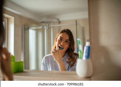 Portrait of a beautiful young woman brushing teeth in the bathroom.