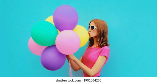 Portrait einer schönen jungen Frau mit bunten Ballons, die sich die Lippen blasen und einen süßen Luftkuss auf blauem Hintergrund senden