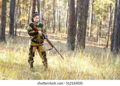 portrait of a beautiful young woman in camouflage clothing with a hunting rifle in the woods, among the grass and pine forest in autumn