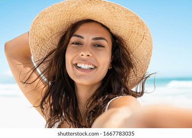 Portrait of beautiful young woman in casual wearing straw hat at seaside. Cheerful young woman smiling at beach during summer vacation. Happy girl with black hair and freckles enjoying the sun. - Powered by Shutterstock