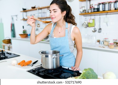 Portrait of beautiful young woman cooking soup with vegetables at home.