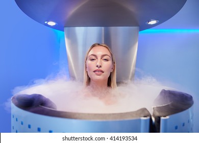 Portrait of a beautiful young woman in cryosauna cabin for whole body cryotherapy. Caucasian female in freezing chamber with nitrogen vapors.