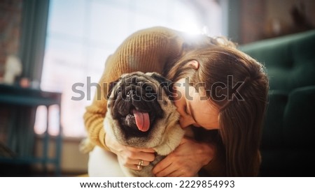 Portrait of Beautiful Young Woman Cuddles Her Adorable Little Pug at Home. Girl Plays with Her Dog, Best Friend. She Pets and Scratches Super Happy Doggy, Have Fun in the Living Room Stockfoto © 