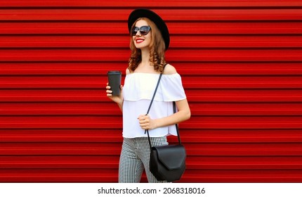 Portrait of beautiful young woman with cup of coffee wearing a black hat on red background - Shutterstock ID 2068318016