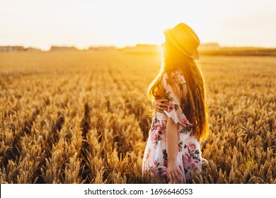 Portrait of a beautiful young woman with curly hair and freckles face. Woman in dress and hat posing in wheat field at sunset and looking at camera. - Powered by Shutterstock