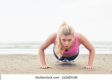 Portrait of a beautiful young woman doing push ups on the beach - Powered by Shutterstock