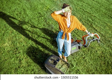 Portrait Of A Beautiful Young Woman Dressed Casually Resting While Cutting Grass With Lawn Mower On The Backyard, View From Above