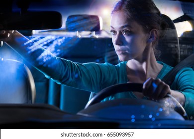 Portrait Of A Beautiful Young Woman Driving Her Car At Night In The Rain, She Adjusts Her Rear-view Mirror