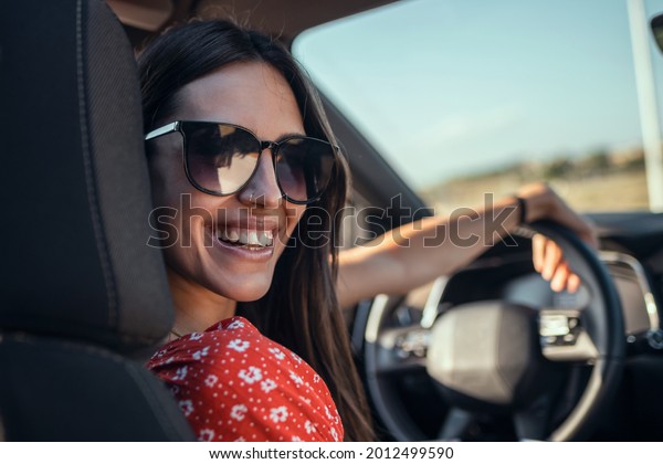 Portrait of beautiful young woman driving a car\
while smiling to the\
camera.