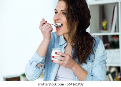 Portrait of beautiful young woman eating yogurt at home.