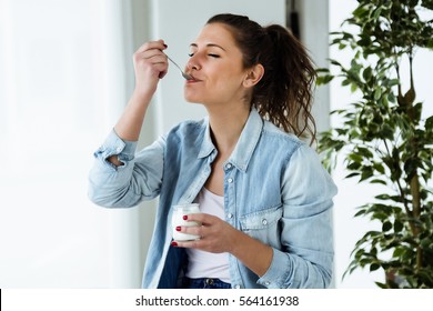 Portrait of beautiful young woman eating yogurt at home. - Shutterstock ID 564161938