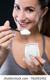 Portrait Of Beautiful Young Woman Eating Yogurt Over Black Background.